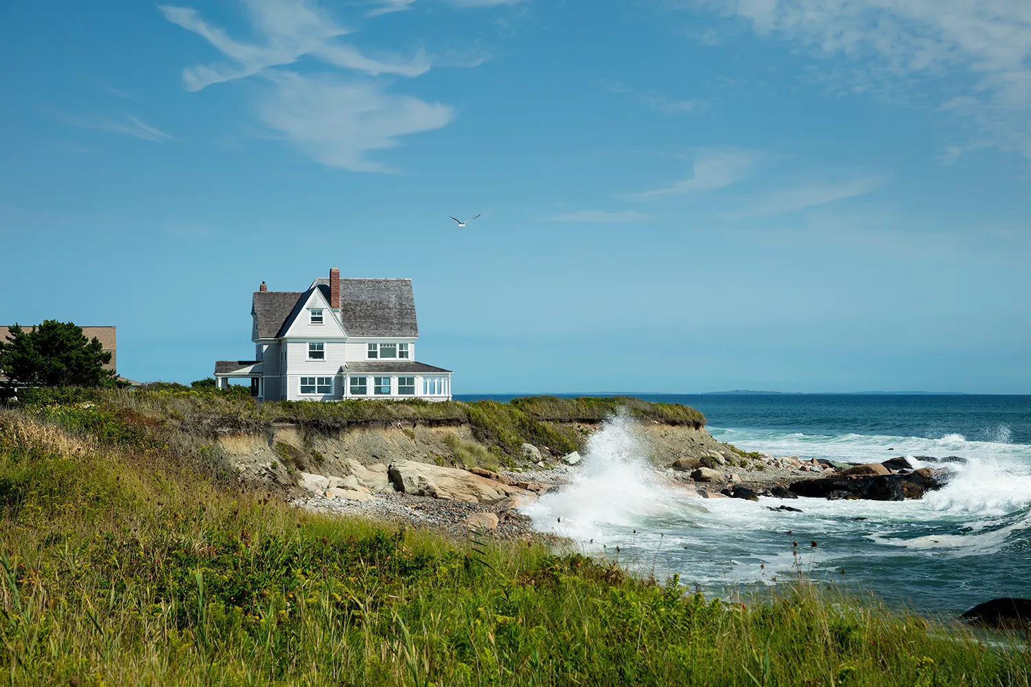 White clifftop cottage above crashing surf along the Little Compton shoreline.