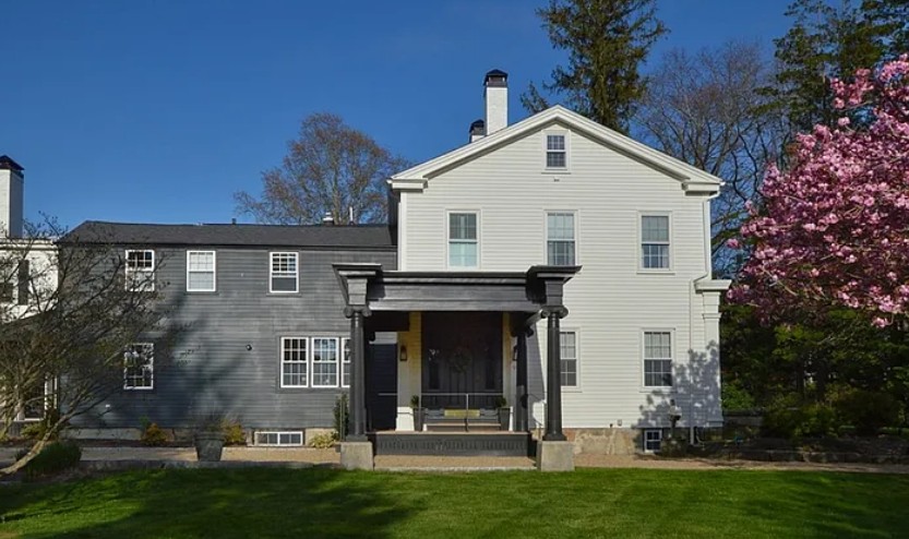 Restored antique home with a black portico and blooming cherry tree on a spring day in New Bedford