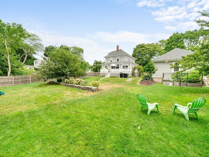 Spacious fenced backyard with green Adirondack chairs behind a South Dartmouth home.