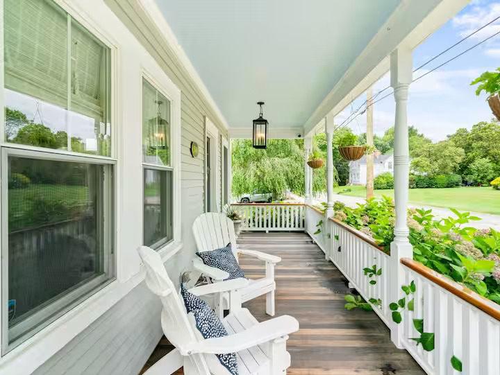 Farmer's porch with white Adirondack chairs and hanging planters on a South Dartmouth home.