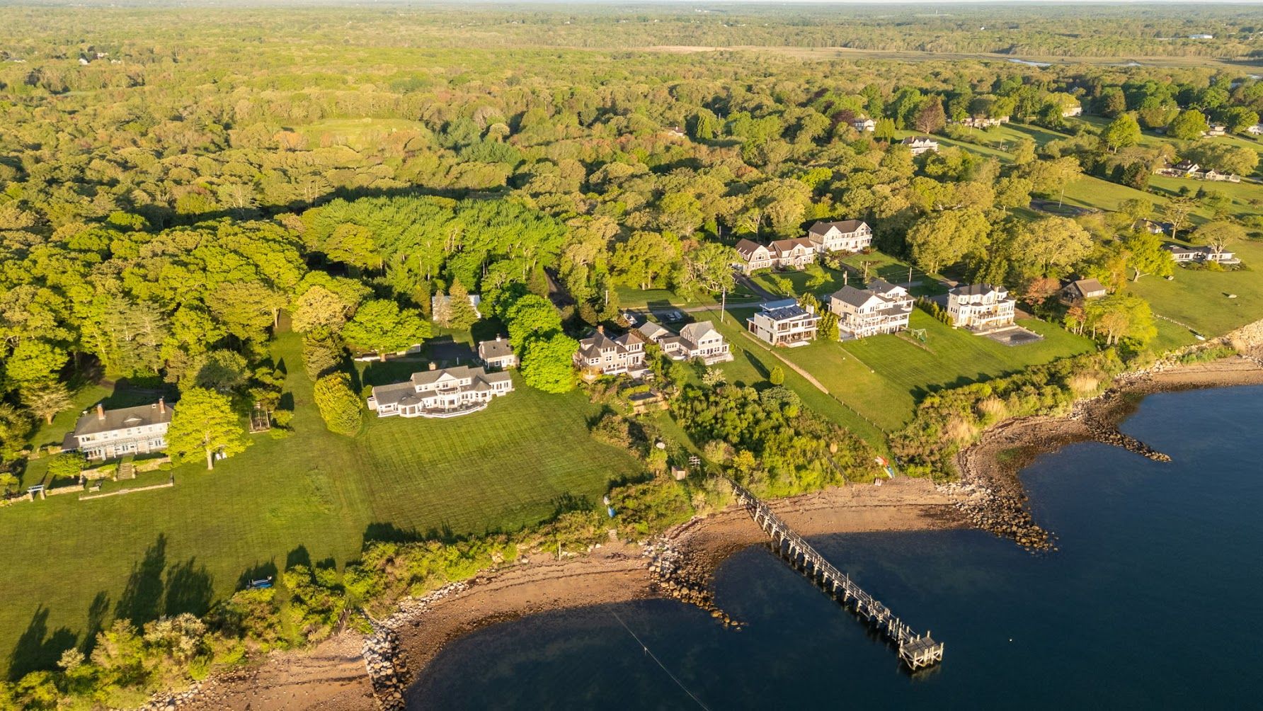Aerial view of shingle-style waterfront homes and a private pier along the shore in Dartmouth.